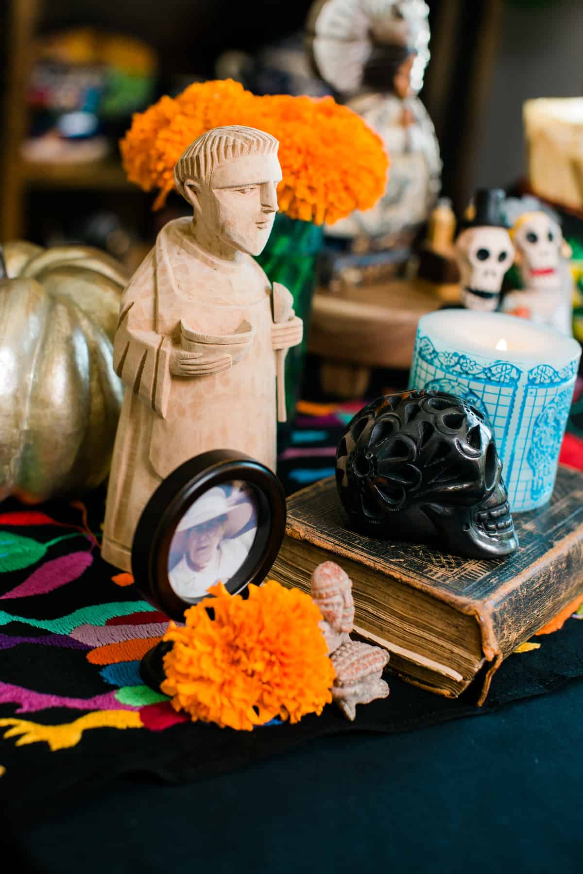 a close-up shot of a a mini alter for Dia de los Muertos adorned with family photographs, candles, marigolds, San Pascual and figurines