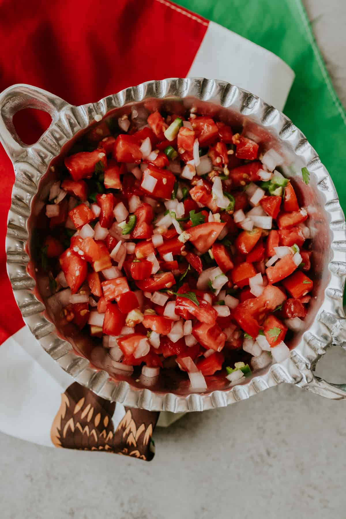 Freshly chopped Pico de Gallo salsa in a silver bowl with a red, white, and green Mexican flag underneath