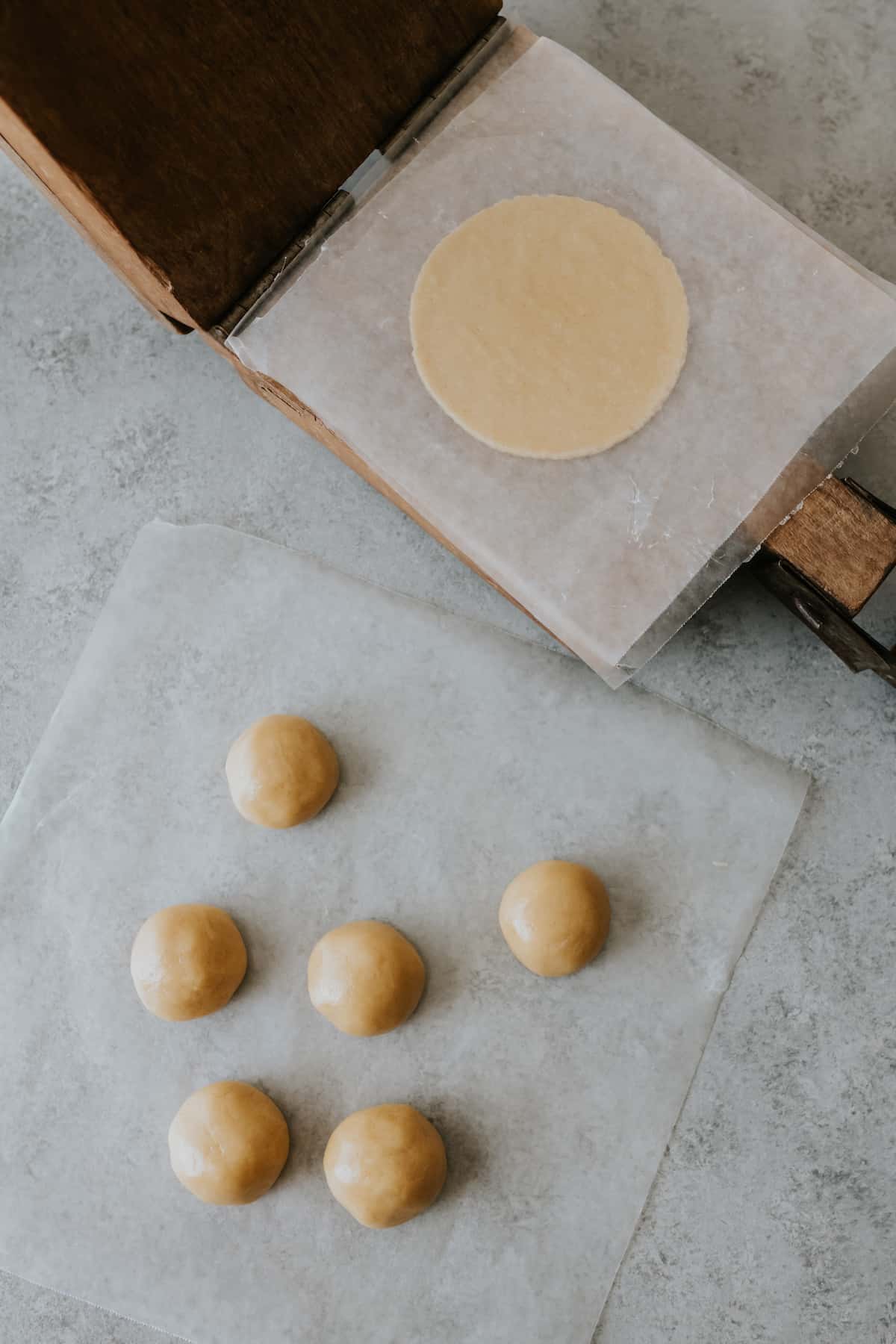 primitive wooden tortilla press with dough balls on wax paper