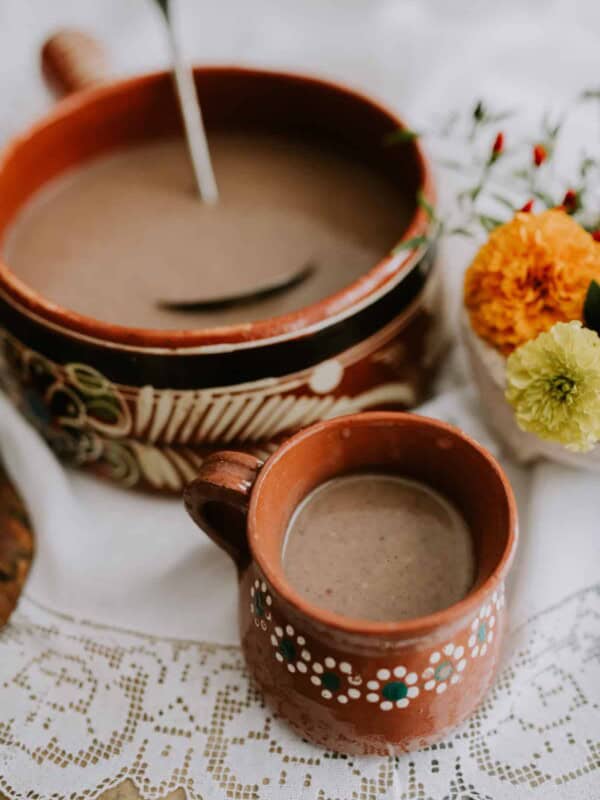 Mexican Hot Chocolate in Mexican barro pot next to a matching mug filled with Mexican hot chocolate.