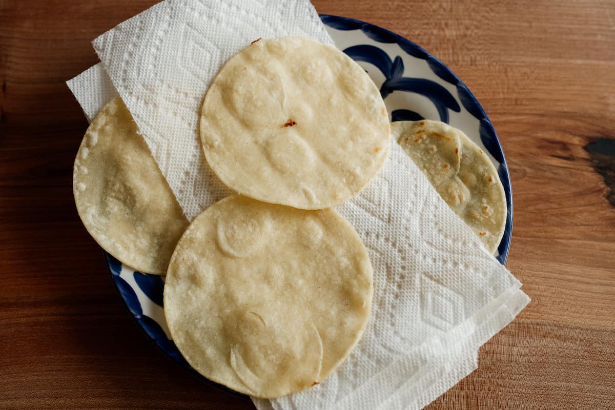 fried corn tortillas draining on a paper towel-lined plate. 