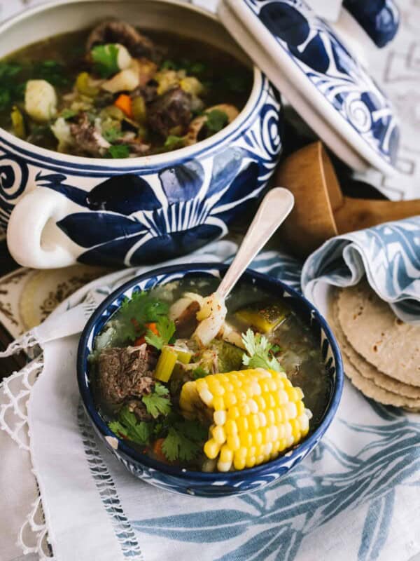 blue and white Mexican soup tureen filled with oxtail soup and a stack of corn tortillas and a wooden ladle.