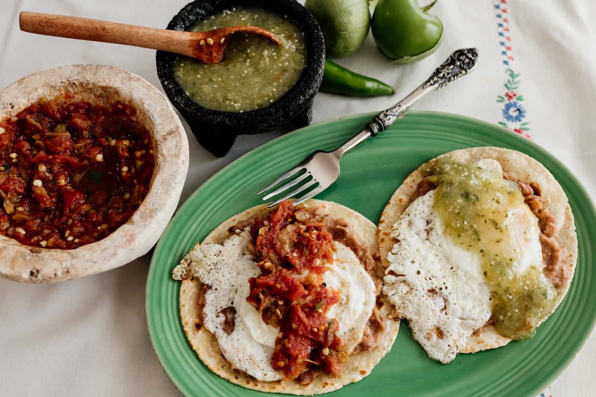 huevos ranchers divorciados on a green plate with two sides of salsas