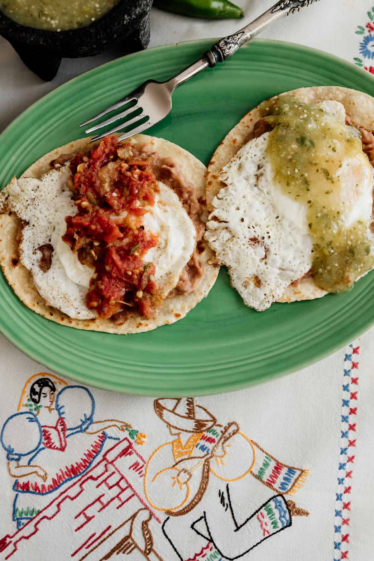 green plate with Huevos Divorciados -- corn tortillas topped with refried beans, eggs, and red and green salsa