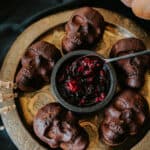 Mexican Chocolate Skull Cakes served on a gold vintage plate with a black bowl of roasted berry sauce in the center.