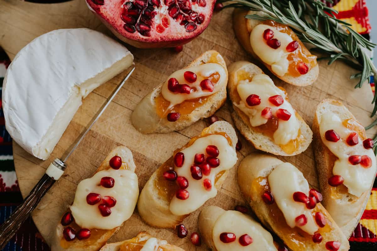 closeup shot of festive brie bruschetta crostini on a cutting board and topped with pomegranate arils for serving as an appetizer.