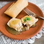 terracotta plate with chicken tamales verdes and a silver fork.