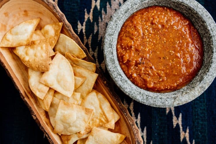 Smoky Roasted Tomatillo-Chipotle Salsa served in a traditional stone molcajete, accompanied by crispy tortilla chips in a carved wooden bowl.