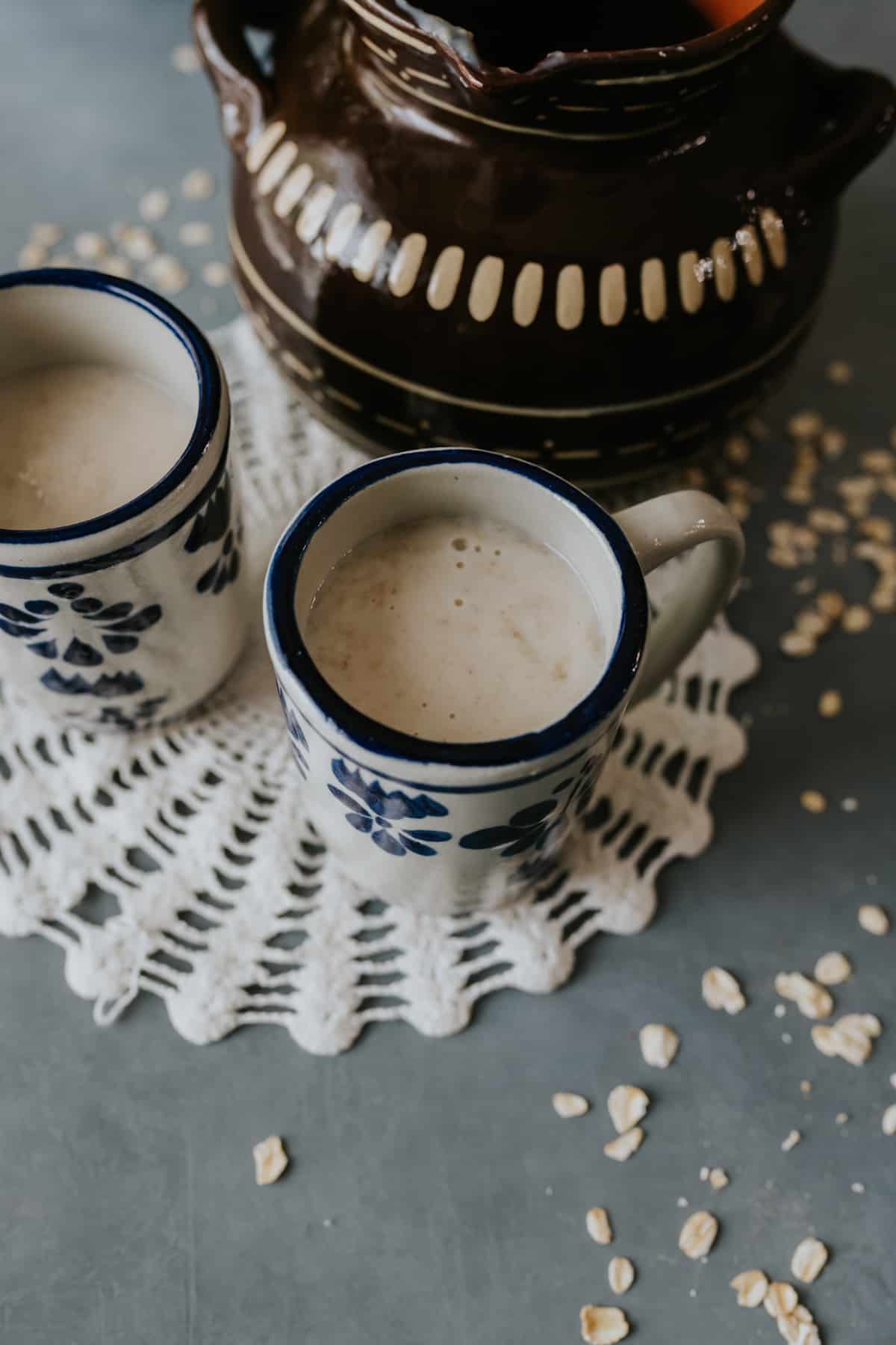 Atole de Avena in two Mexican blue and white cups with a doily and cazuela