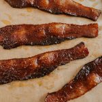 Spicy Maple Candied Bacon strips cooling on brown parchment paper.