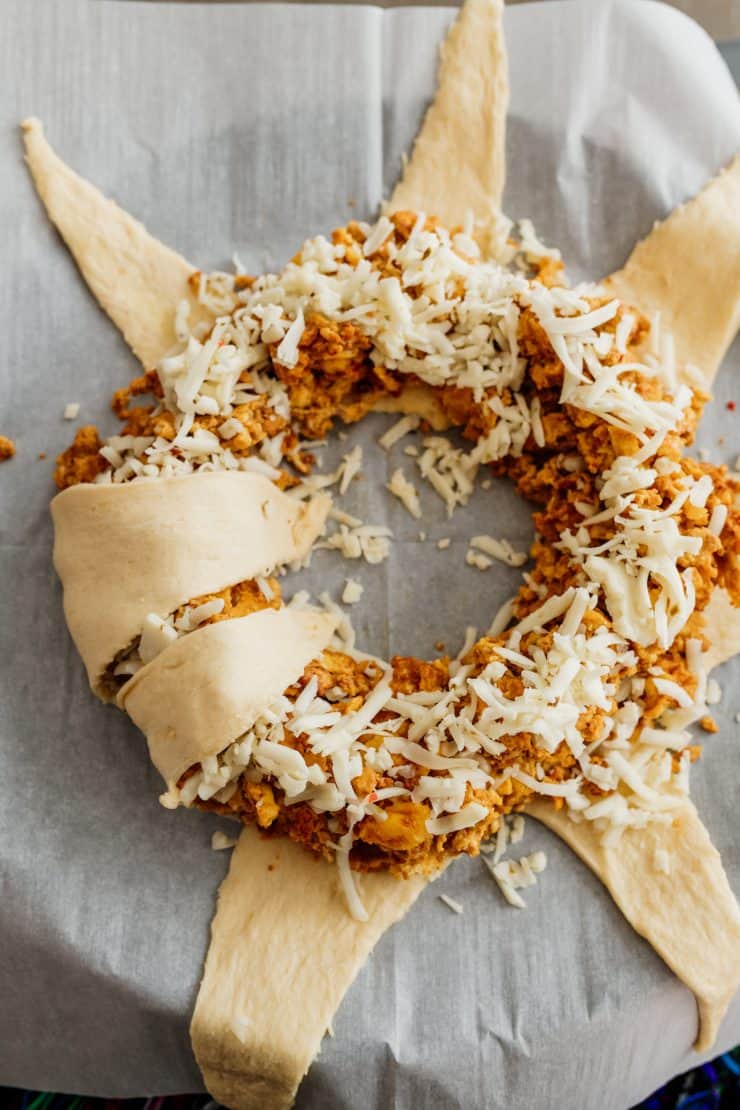 Crescent dough triangles partially folded over a ring of chorizo and eggs topped with shredded cheese, forming the breakfast wreath before baking.