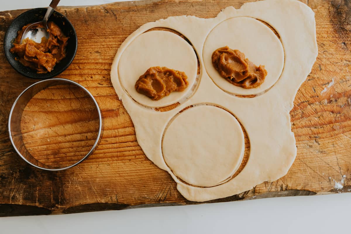 process shot showing rolled out empanada dough cut into circles with dollops of sweet potato filling added on one half of each of the circles.