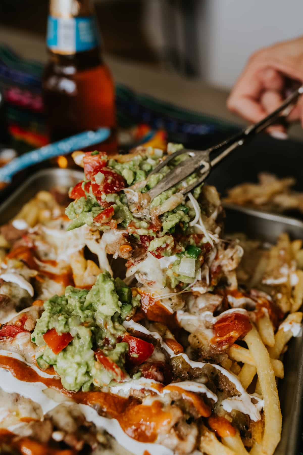 loaded fries being served using vintage tongs. Toppings include guacamole and salsa ad melted cheese.