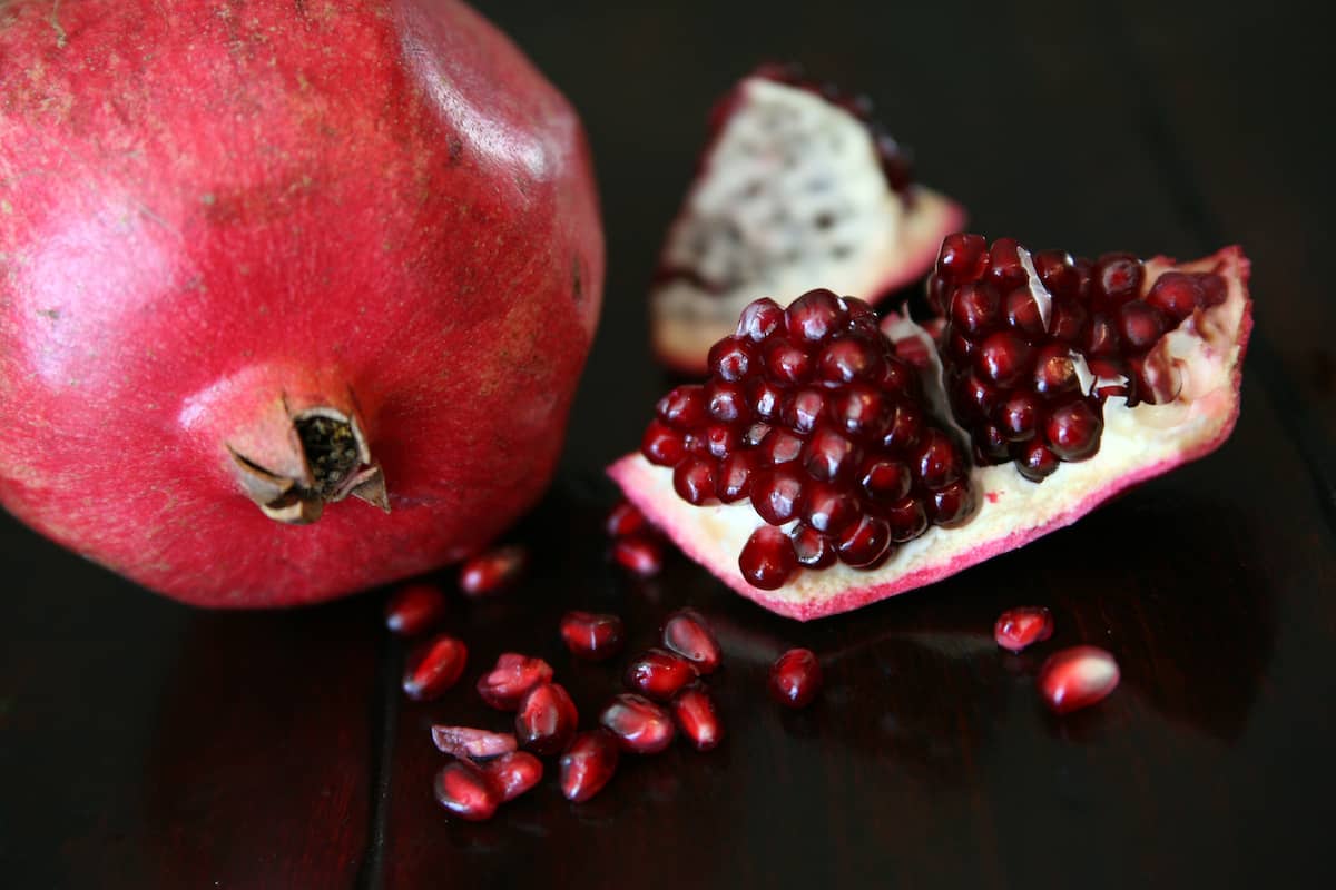 whole pomegranate next to a halved pomegranate with the arils spilling onto a black table.