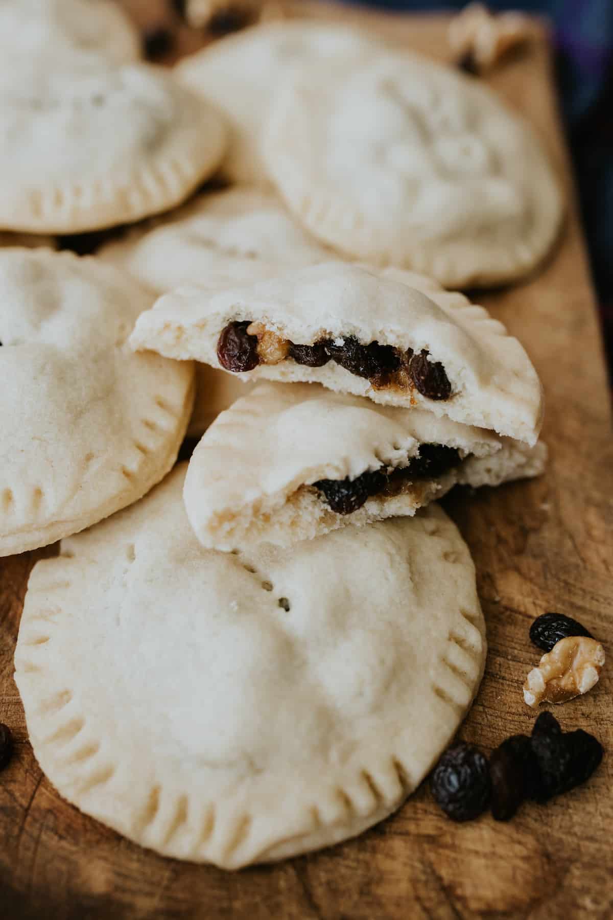 a closeup of a raisin filled cookie sliced in half to show fruit and nut filling on top of other freshly baked raisin filled cookies on a wooden cutting board