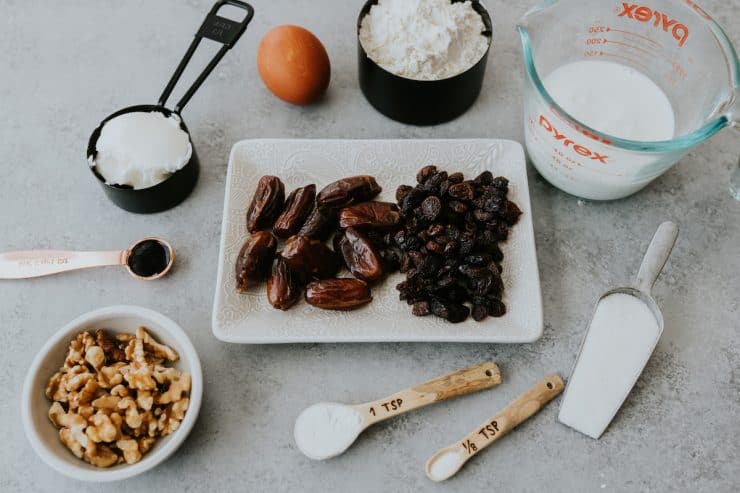Overhead view of ingredients for Raisin Filled Cookies arranged in white bowls and clear measuring dishes, ready for holiday baking.