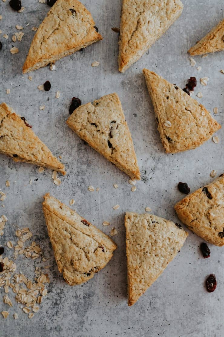 Cranberry Maple Oatmeal Scones arranged on a gray background with scattered oats and dried cranberries for a rustic fall look.