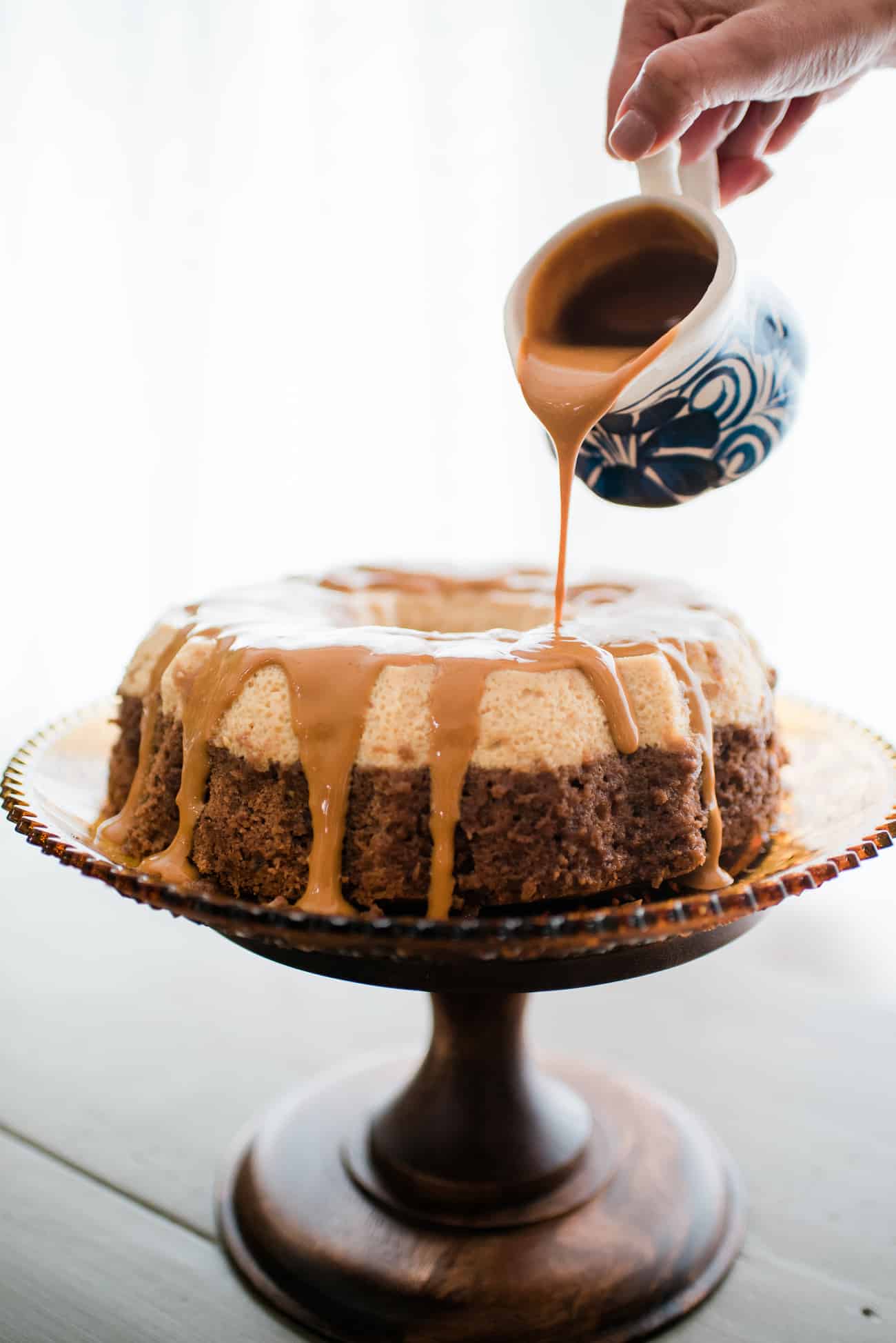 Side view of chocoflan on a cake stand being drizzled with dulce de leche.