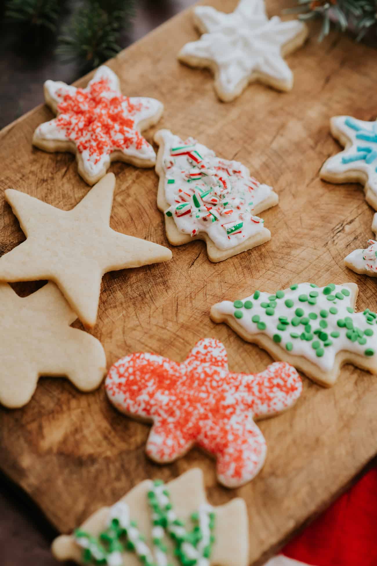 wooden cutting board with soft cream cheese sugar cookies, some of which have been decorated with frosting and sprinkles.