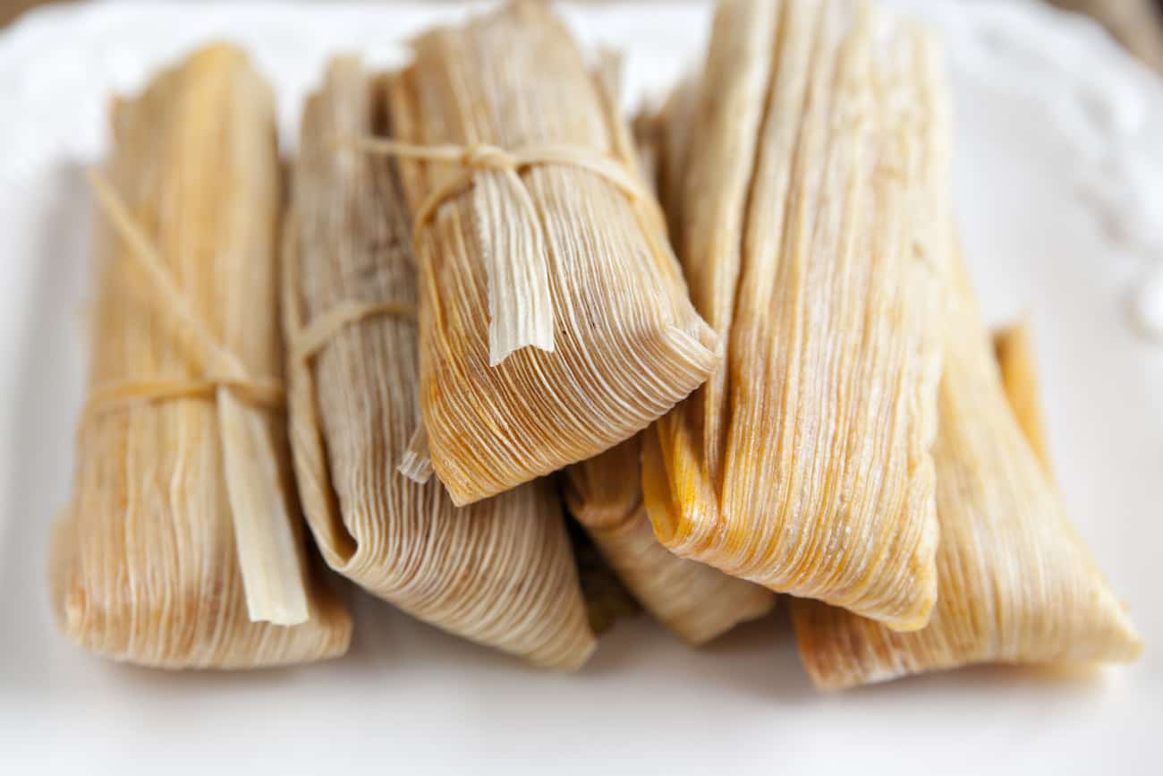 pile of wrapped tamales in corn husks on a white dinner plate.