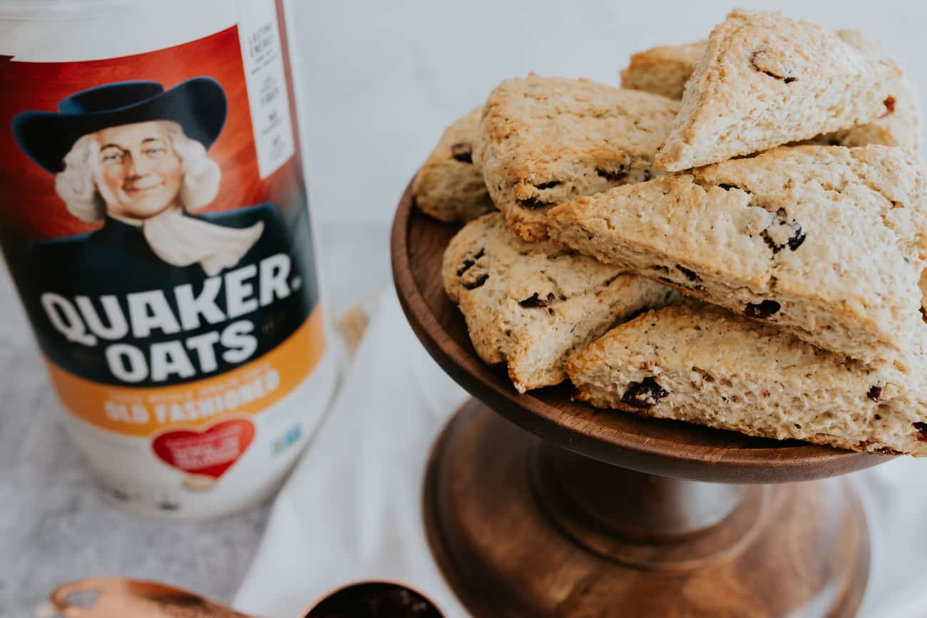wooden pedestal of cranberry maple oatmeal scones with a canister of quaker oats in the background.
