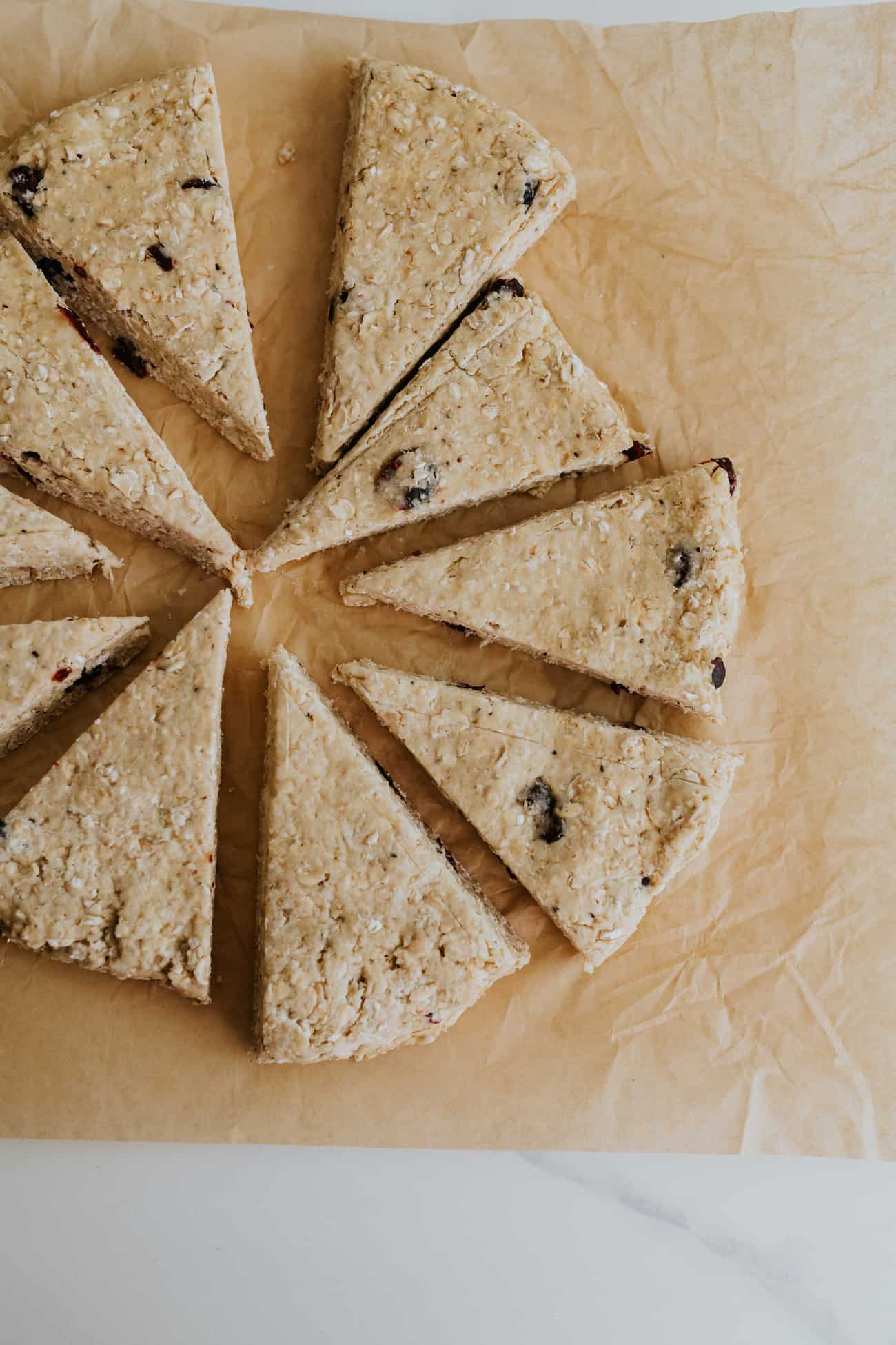 cranberry maple oatmeal scones on a piece of parchment paper after rolling and cutting into wedges.