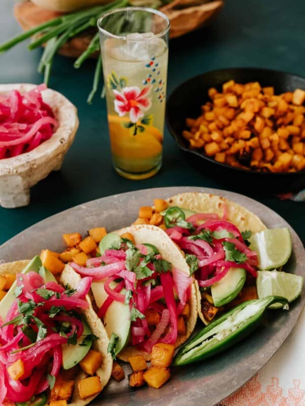 tablescape with sheet pan roasted butternut squash tacos, a bowl of pickled red onions, and an orange spritz in a hand painted collins glass.