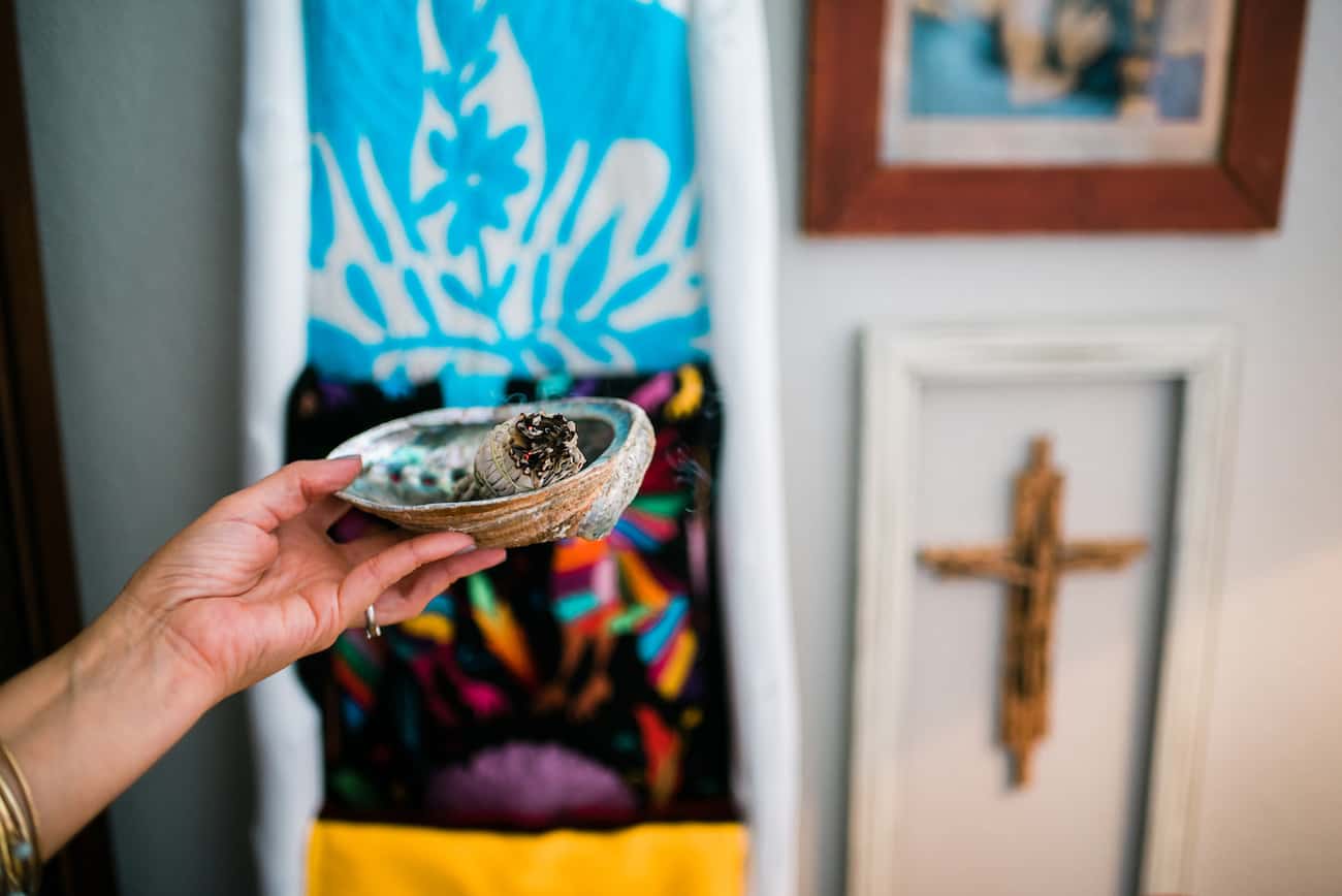 a hand holding an abalone shell filled with a smoking smudge stick to smudge her home.