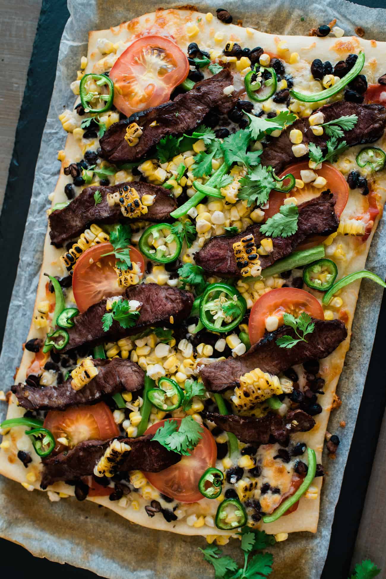 Overhead shot of Carne Asada and Roasted Corn Taco Pizza on a metal sheet.