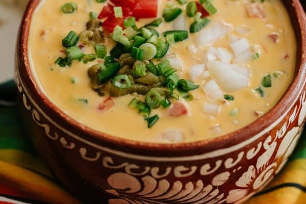 tex mex style chile con queso in a brown bowl with a serving handle.