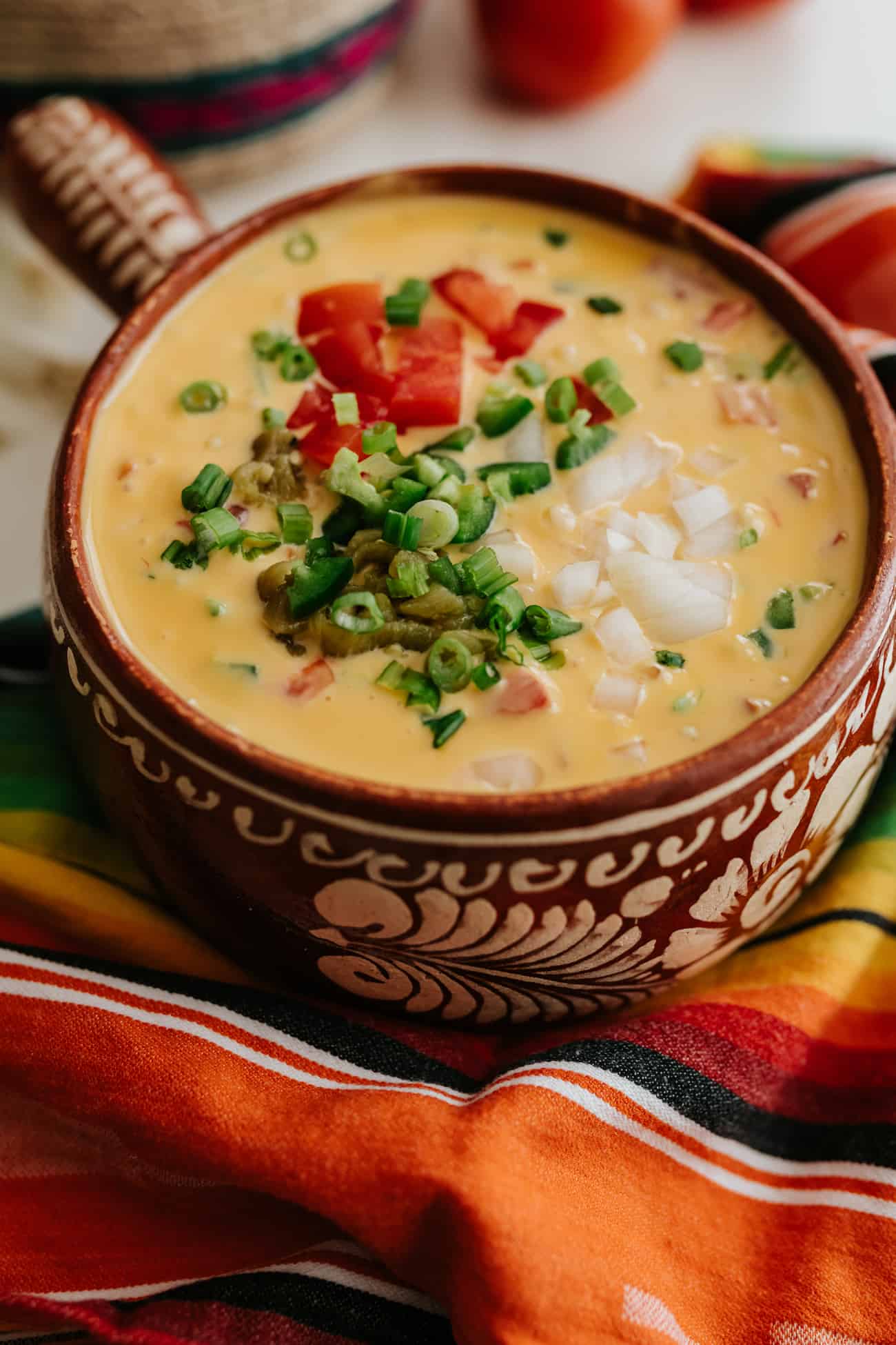 close up shot of chile con queso garnished with green onions, roasted green chiles, tomatoes and onions.
