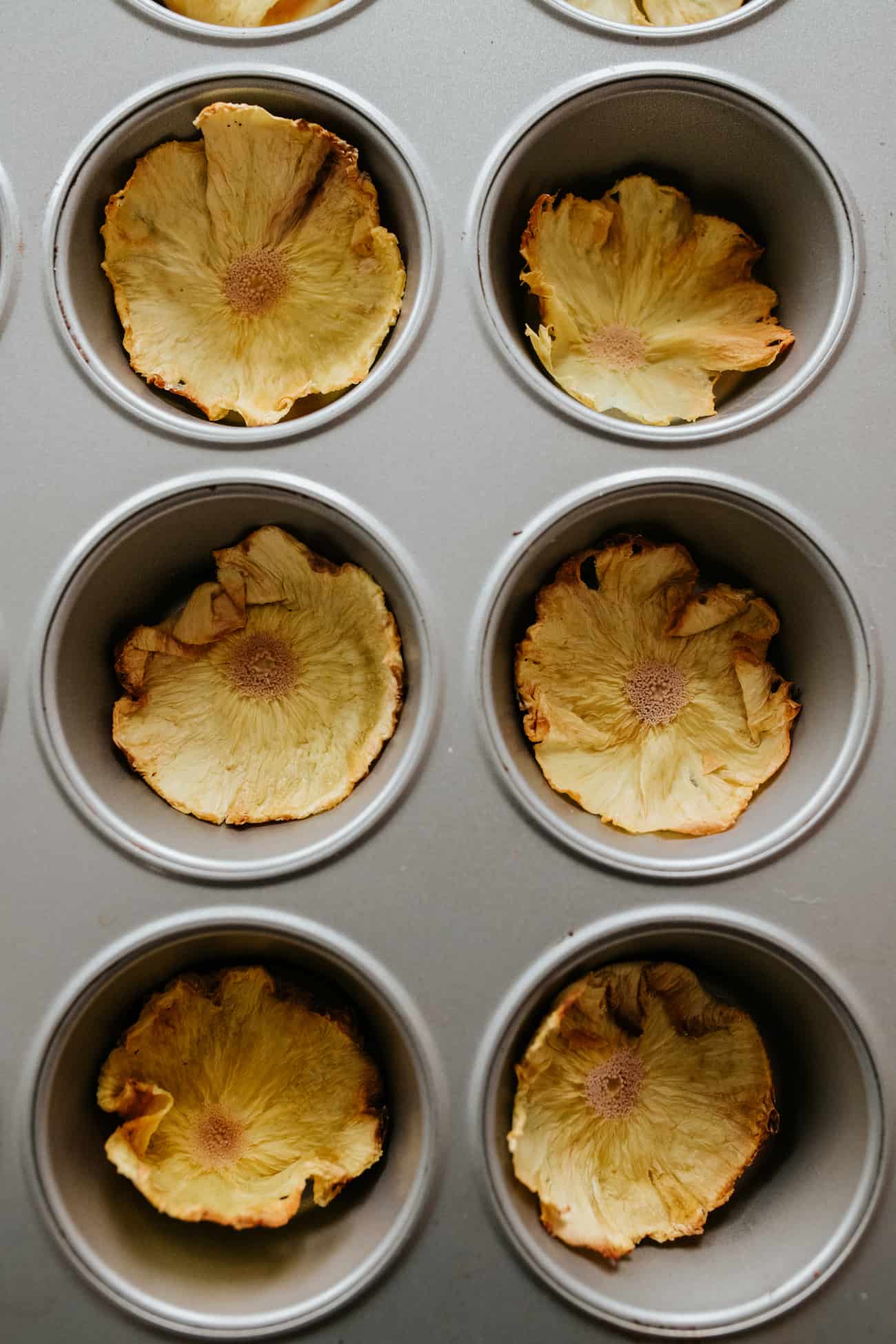 dried pineapple flowers being shaped in muffin tins.