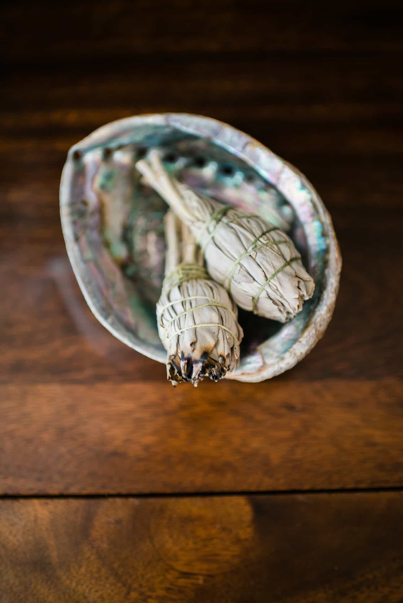 how to smudge your home using a homemade smudging stick in a bowl lightly lit with smoke coming out, all on a wooden table