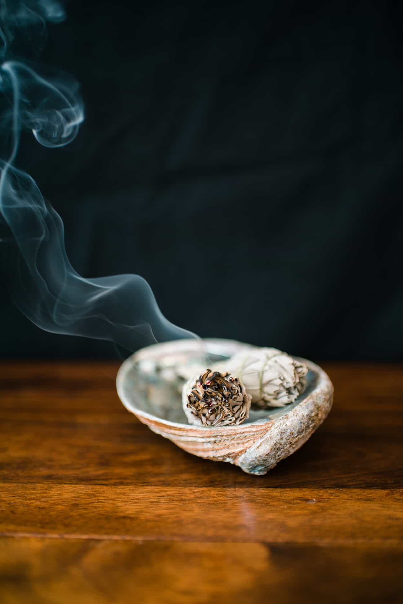 how to smudge your home using a homemade smudging stick in a bowl lightly lit with smoke coming out, all on a wooden table