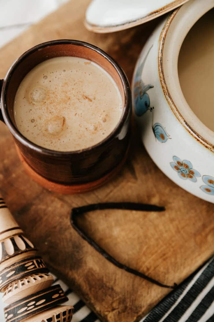 mug filled with atole de vainilla in a brown mug on a wooden board with a vanilla bean.