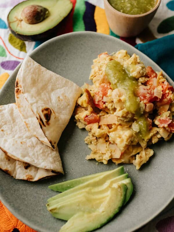 migas on a grey plate with avocado slices and toasted flour tortillas for making breakfast tacos.