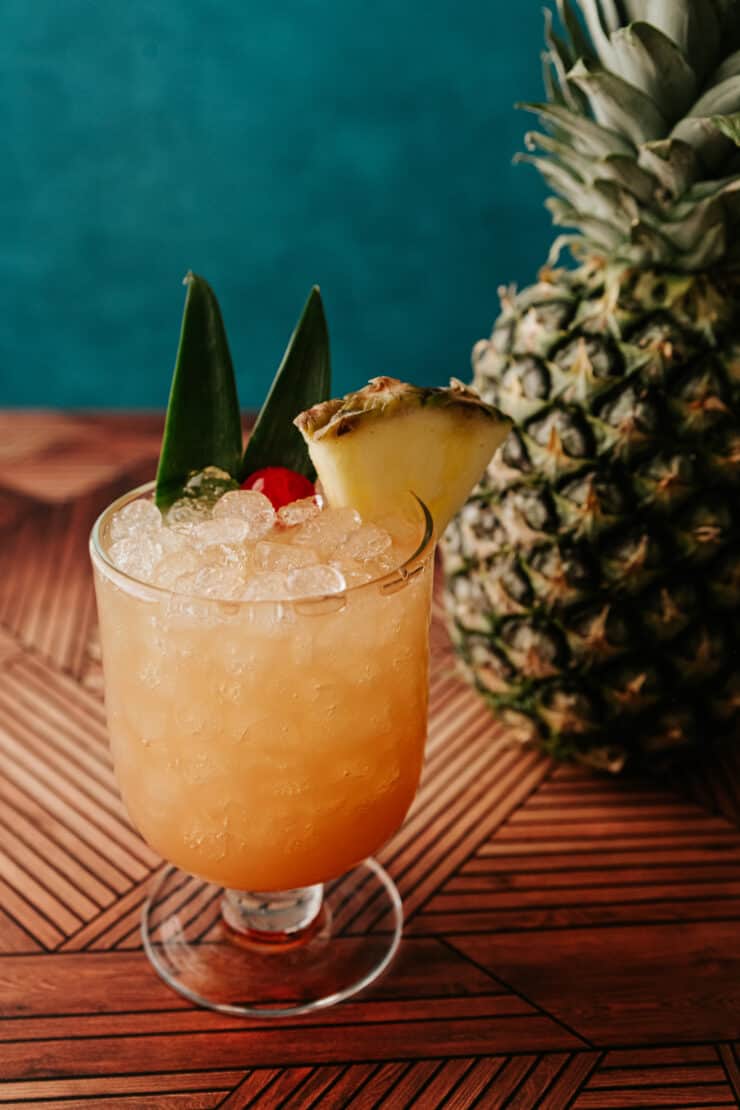 Skinny Hawaiian Mai Tai in a glass over pellet ice garnished with pineapple wedge, maraschino cherry and two pineapple leaves.