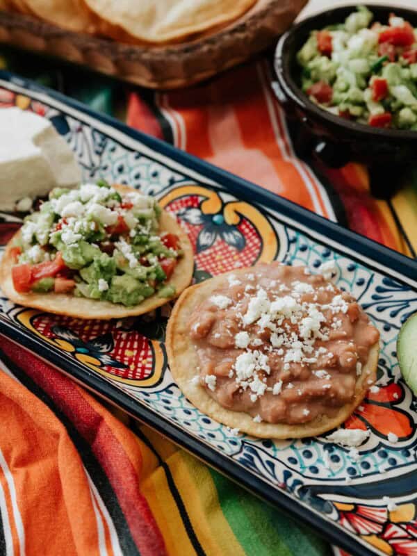 Vegetarian Mexican Tostadas With Refried Beans & Guacamole on a Mexican talavera platter on a striped fabric.