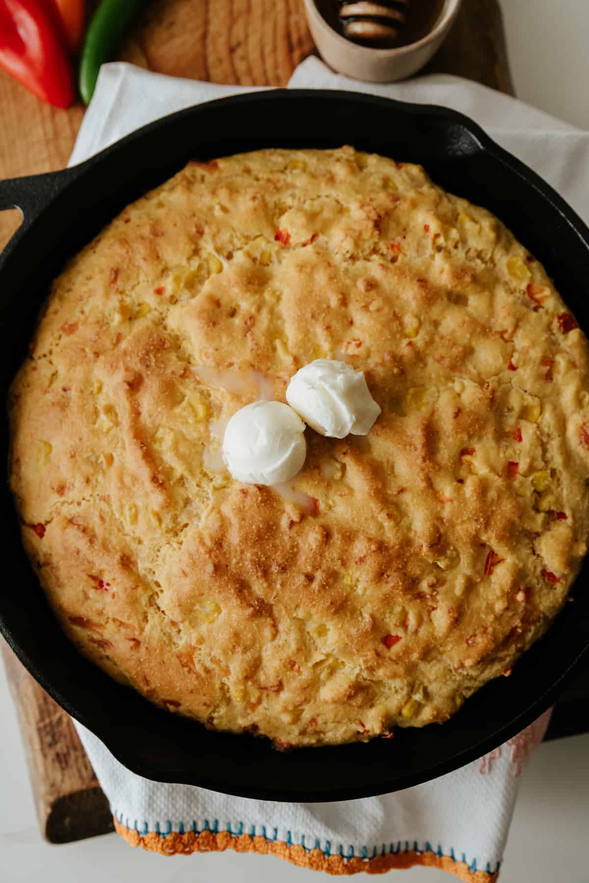 Overhead shot of cheesy cornbread in a skillet with two small balls of butter melting on top.