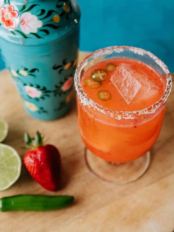 strawberry jalapeno margarita in a clear footed glass with a turquoise floral cocktail shaker in the background.