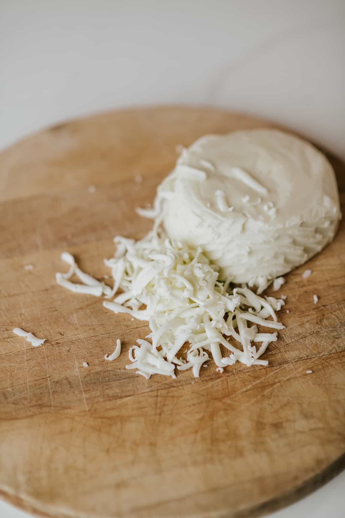 ball of quesillo cheese that has been partially grated on a wooden cutting board.