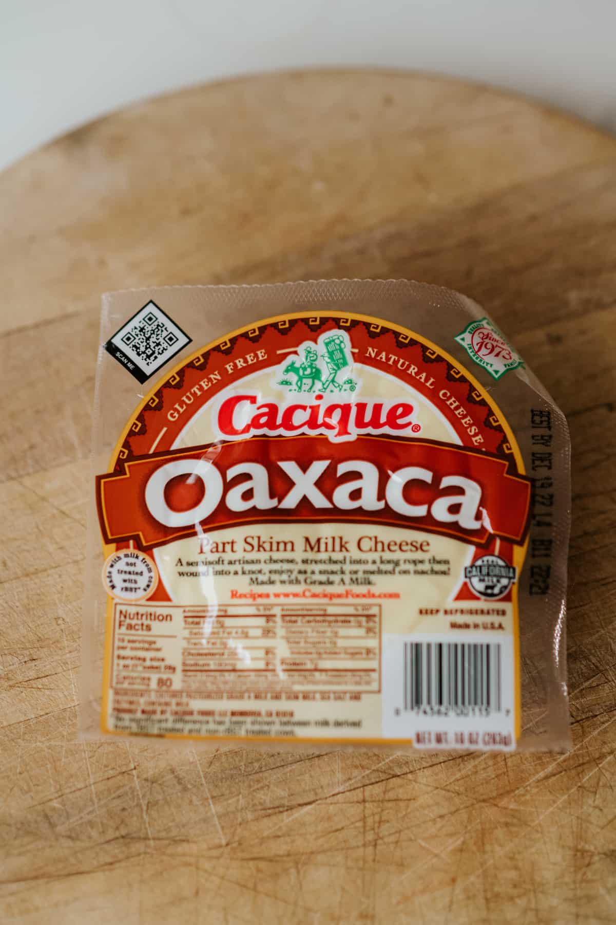 package of cacique brand oaxaca cheese on a wooden cutting board.