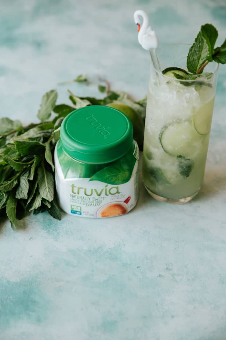 cucumber mint mojito on a table with a container of truvia original sweetener and a bunch of fresh mint. 