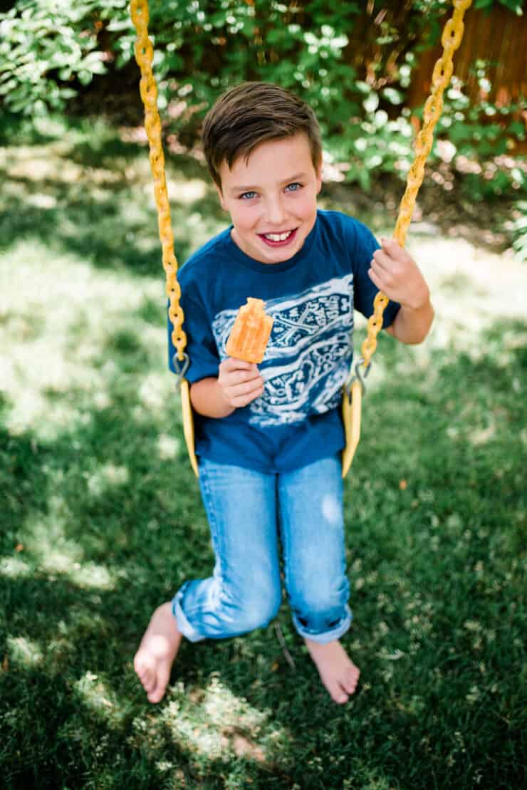 Young boy on a swing holding a chili Mango paleta and smiling. 