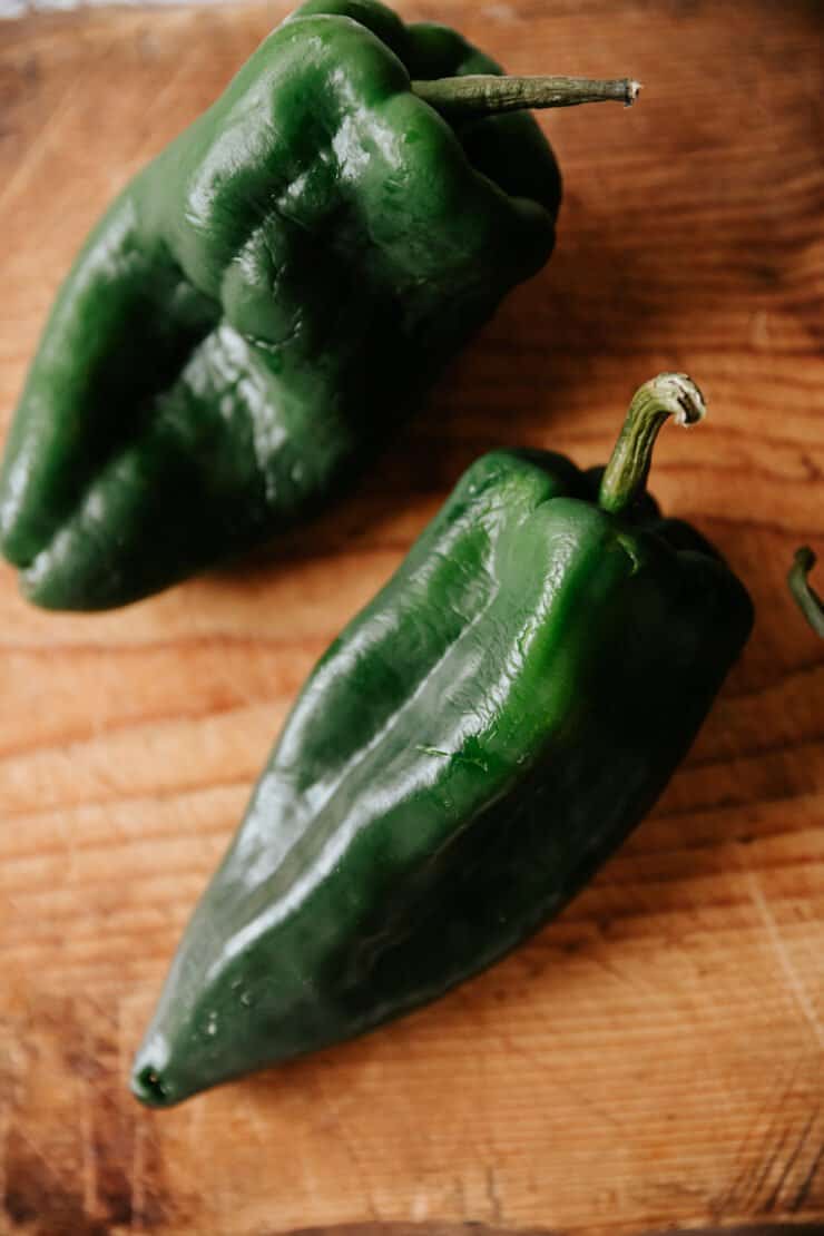 Three fresh poblano peppers on a wooden cutting board before being roasted for Chiles en Nogada.