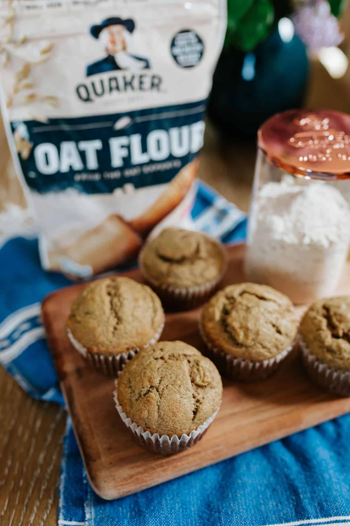 5 banana muffins on a cutting board with a bag of quaker oat flour in the background.