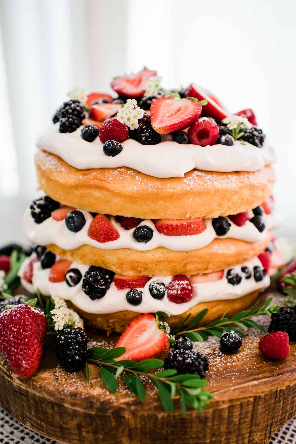 three layer naked cake topped with whipped cream and fresh berries.