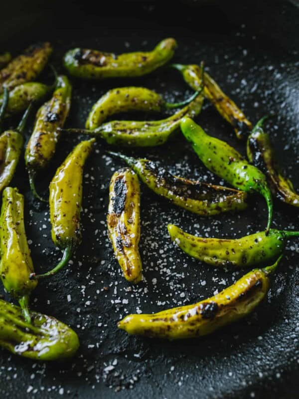 Blistered Shishito Peppers with sea salt in a cast iron skillet.