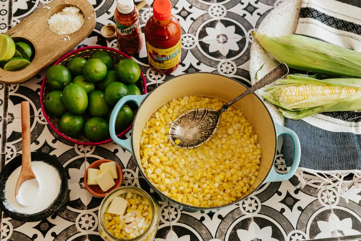 ingredients for making esquites Mexican corn salad laid out on black and white patterned tiles. 