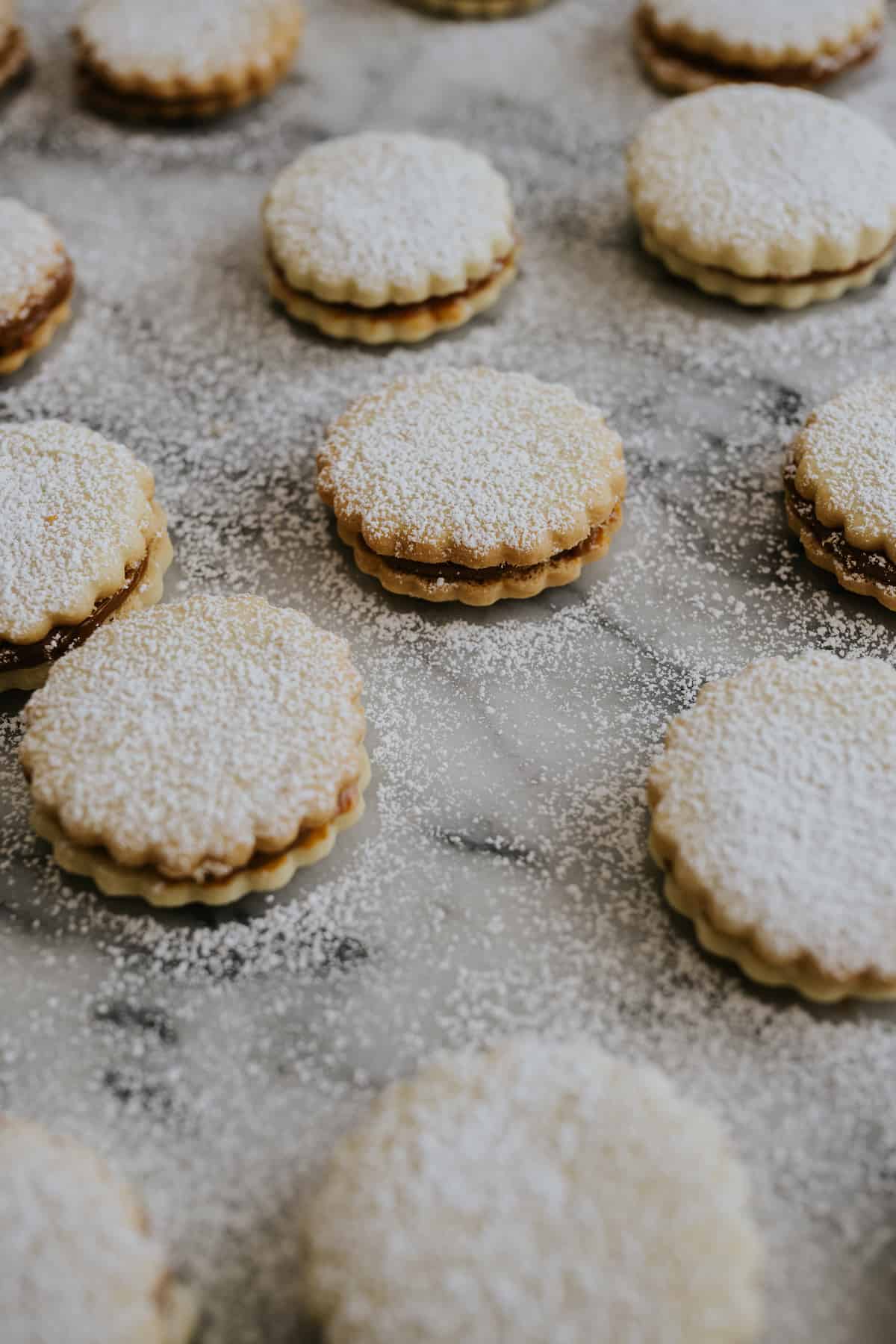 assembled alfajores on a marble slab after being dusted with powdered sugar.